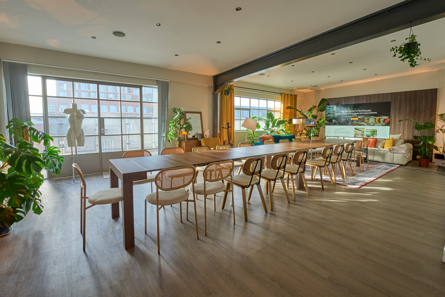 Boardroom-style meeting setup with long table, presentation screen, and natural daylight in the penthouse