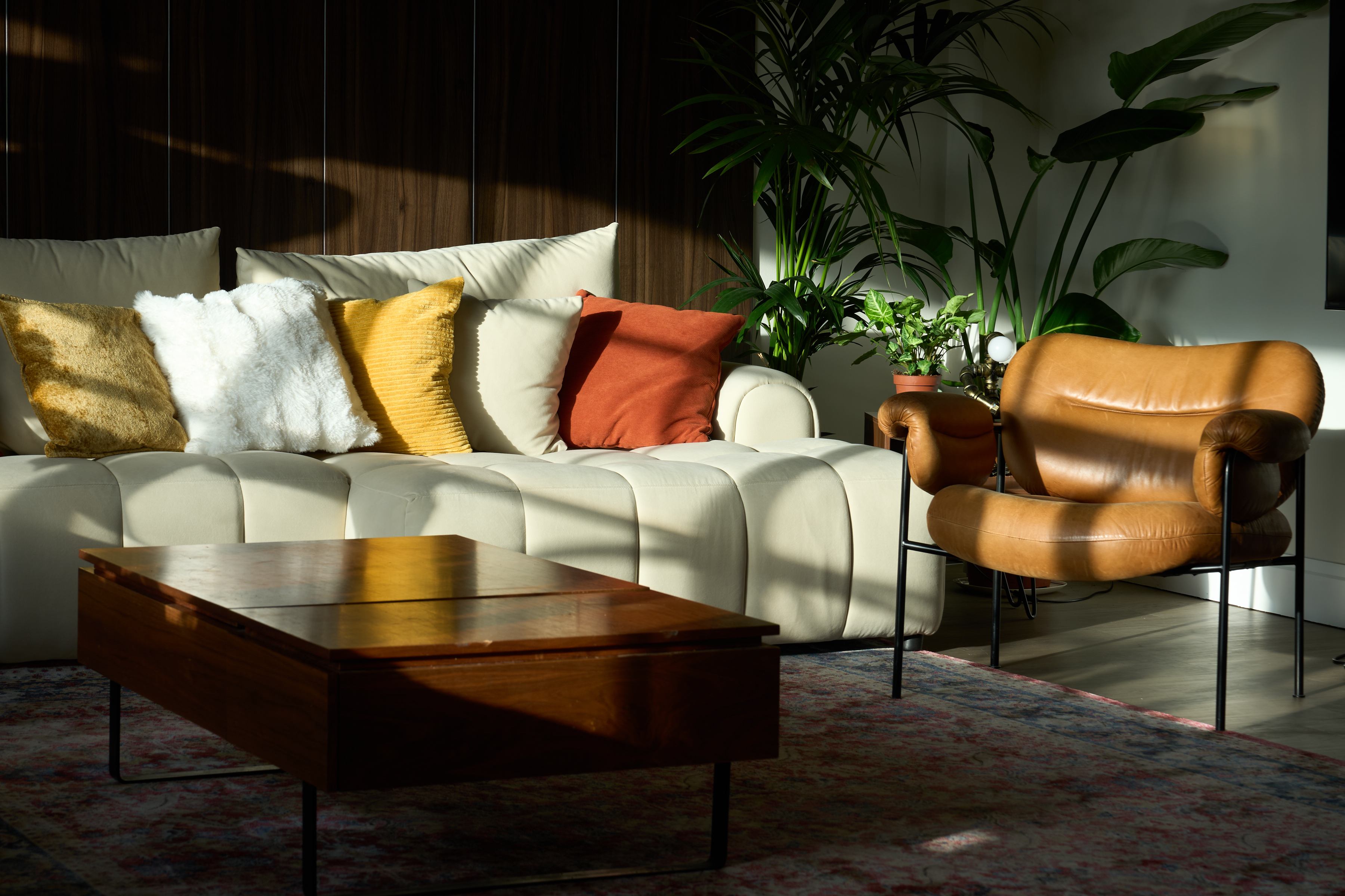 Late-afternoon light across the cream sofa, tan leather chair, and Persian rug in the lounge at The Designer's Penthouse, Old Street London
